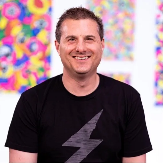 Avi Spivack smiling in front of Nataly's colorful paintings